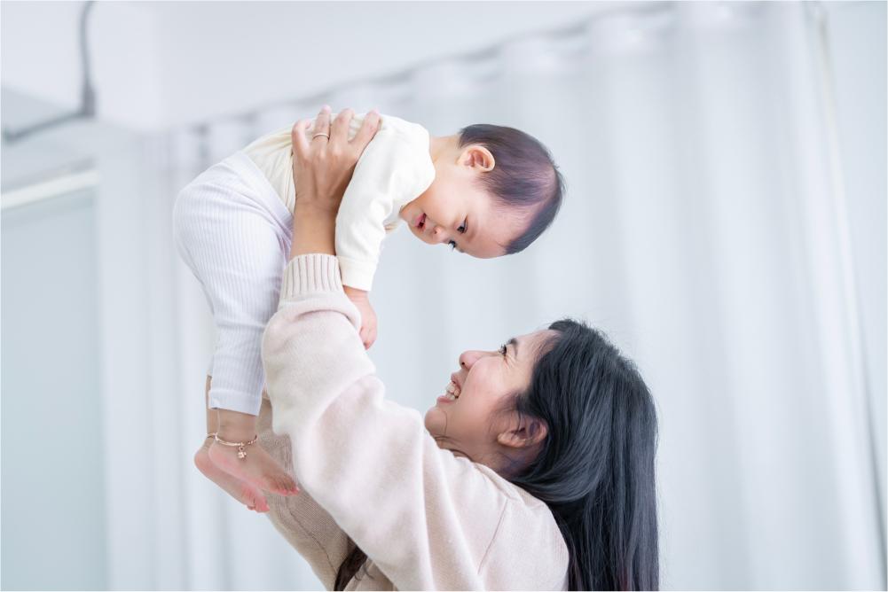 Mom holding baby up in the air smiling with love.