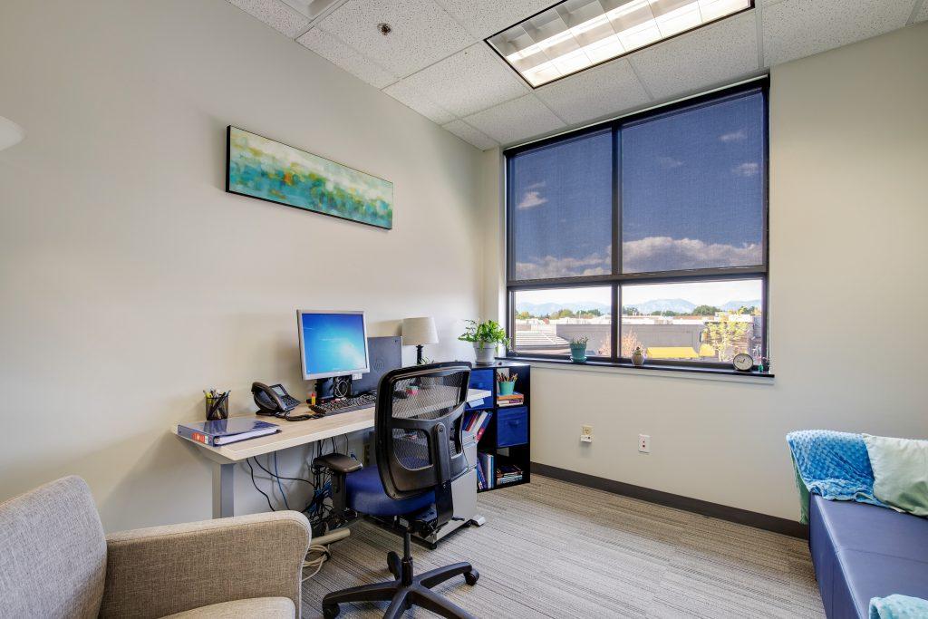 Office with desk, chair, couch, and lounge chair. Tan walls with window.