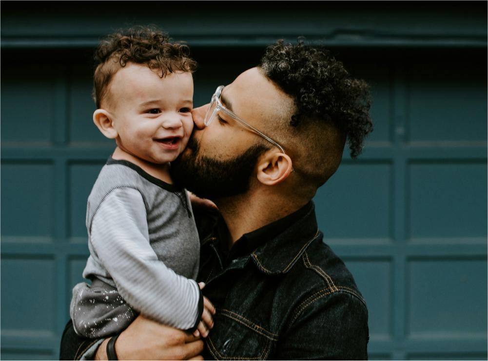 Dad holding toddler kissing on the check.