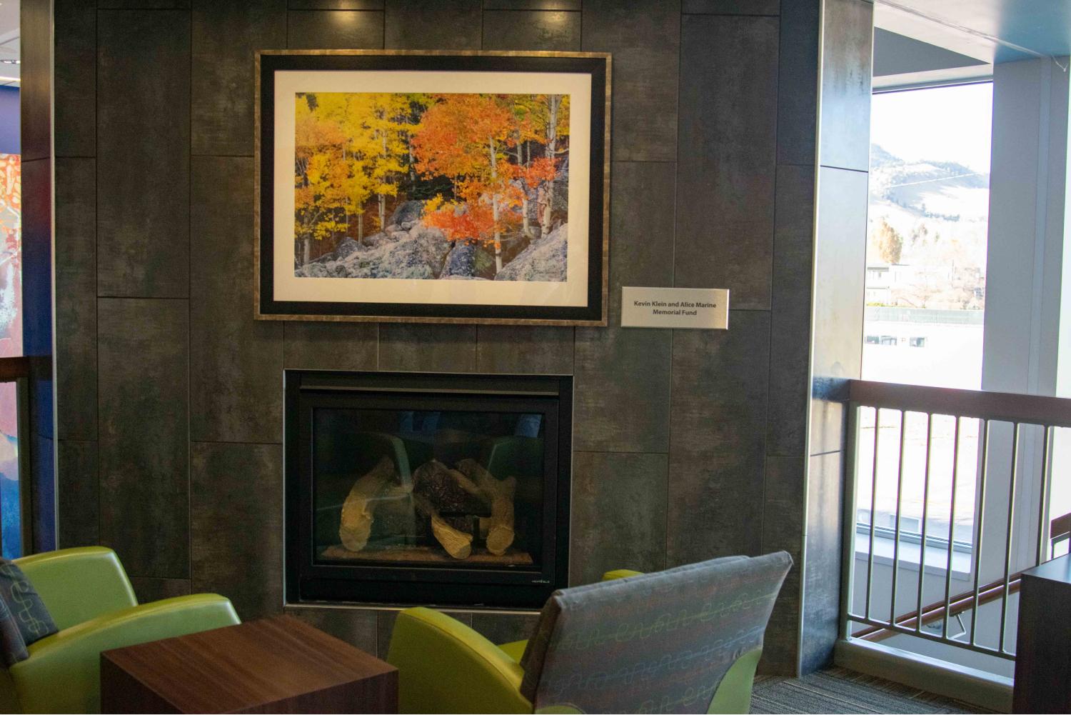 Ryan Wellness Center Upstairs, fireplace with photo of autumn scene. Two green lounge chairs facing fireplace.