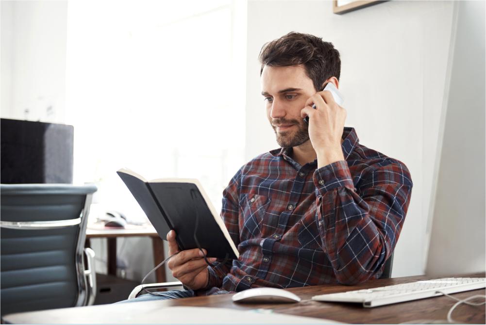 Man looking at planner while on phone.