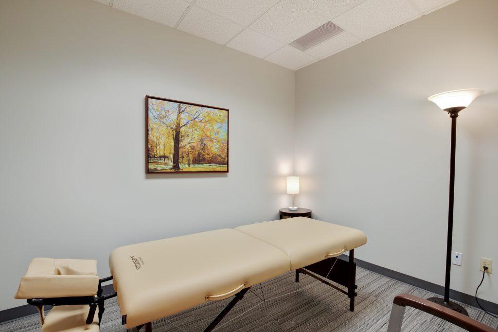 Massage room with massage table, lamps, and tree artwork.