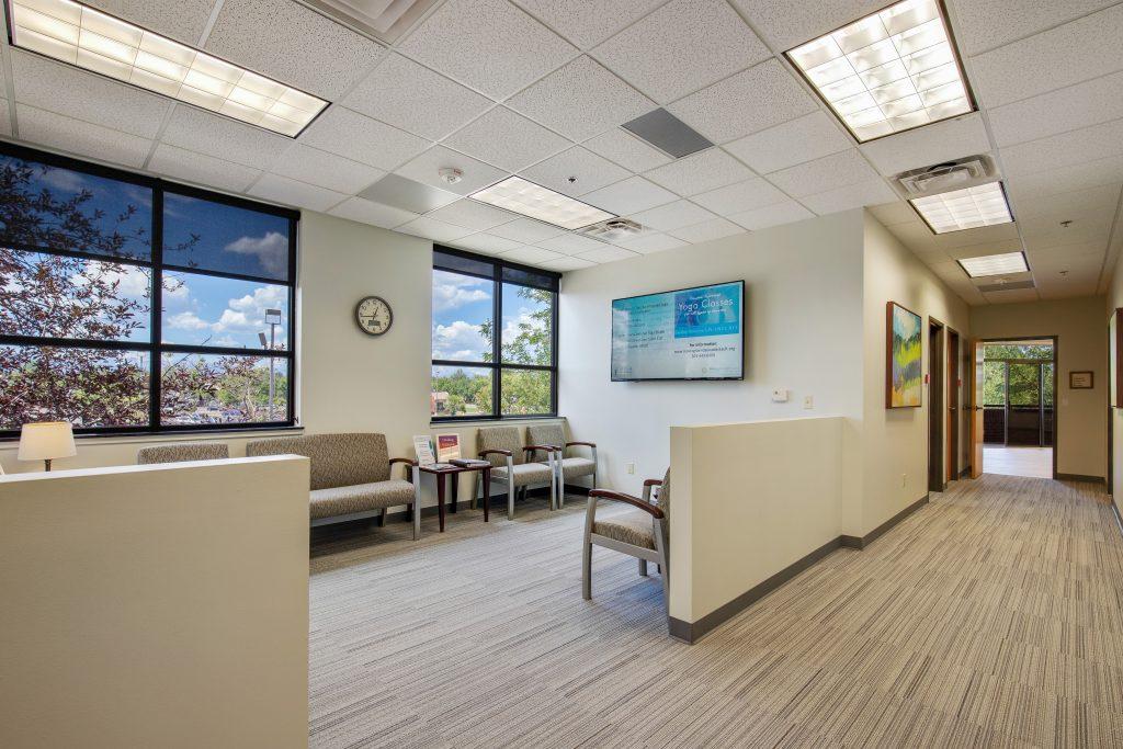 Waiting room with chairs lined up against wall with large windows.