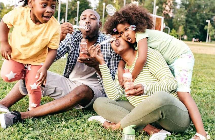 Family at a park playfully blowing bubbles.