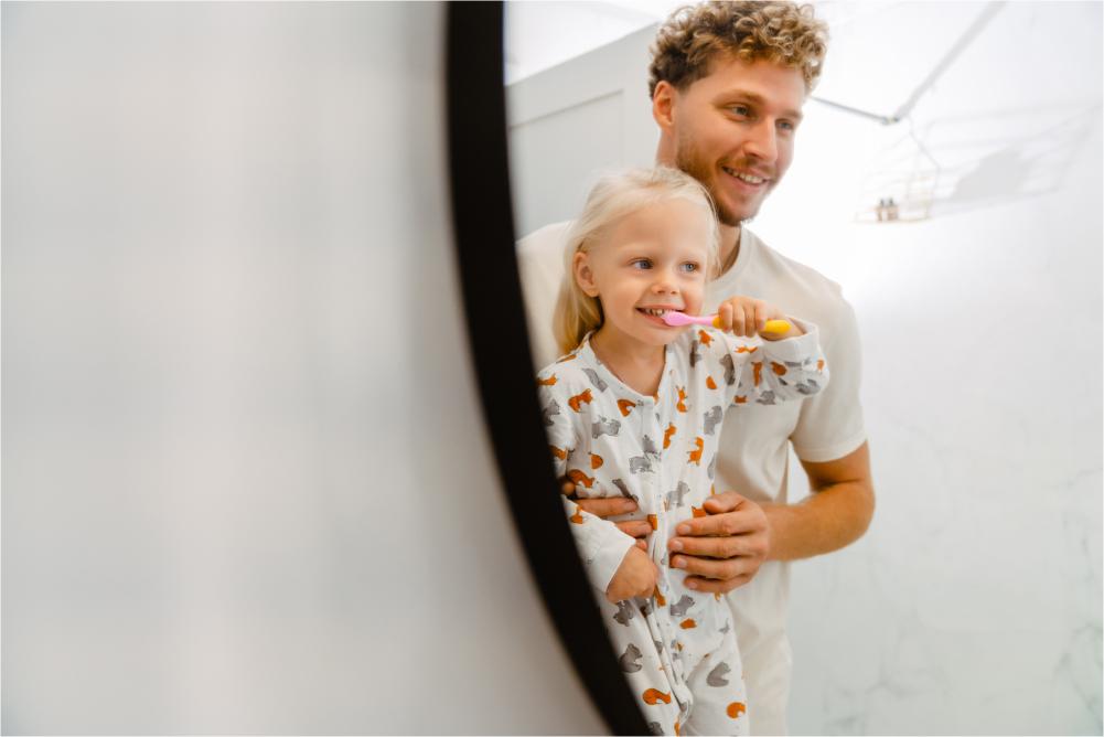 Dad and daughter looking in mirror, daughter brushing teeth.