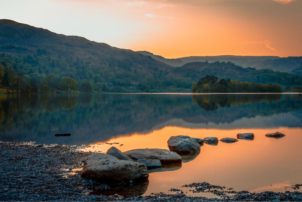 Pathway to Wellness Tile 3: Sunset on lake with trial of rocks.