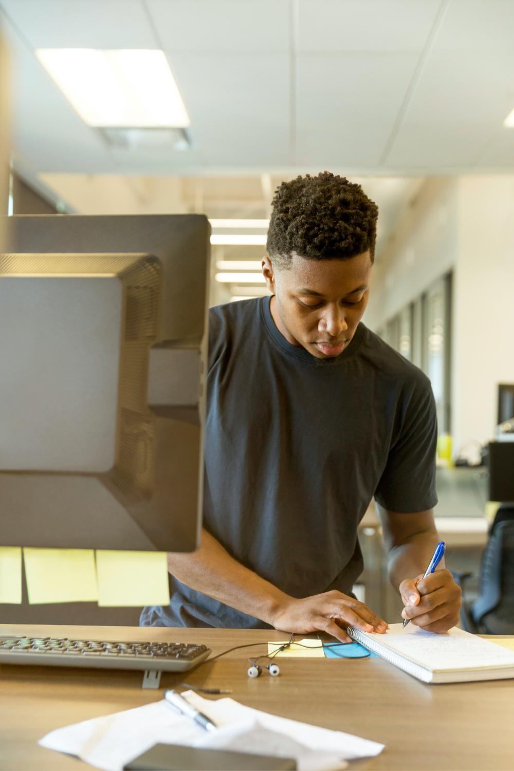 Man taking notes while standing near computer.