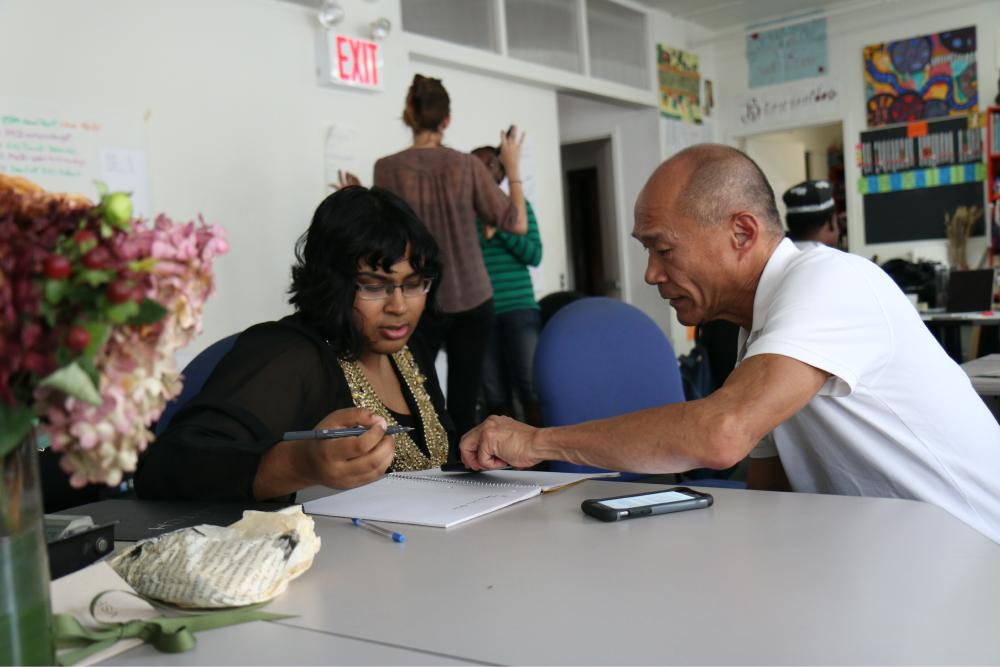 Housing Case Management Tile: People working on paperwork while sitting down at a table.