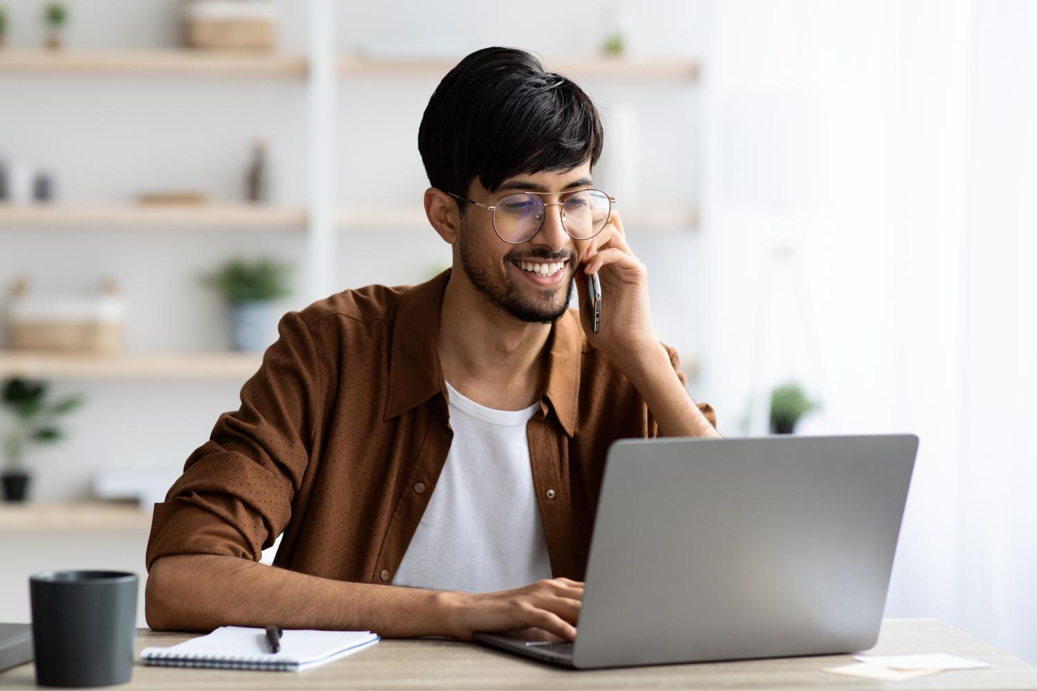 Cheerful man with laptop having phone conversation.