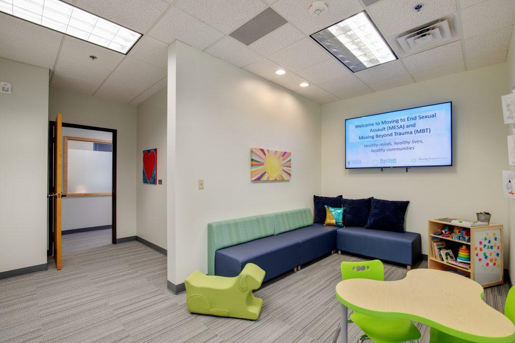 Waiting room with large couch, screen, and children's play table.