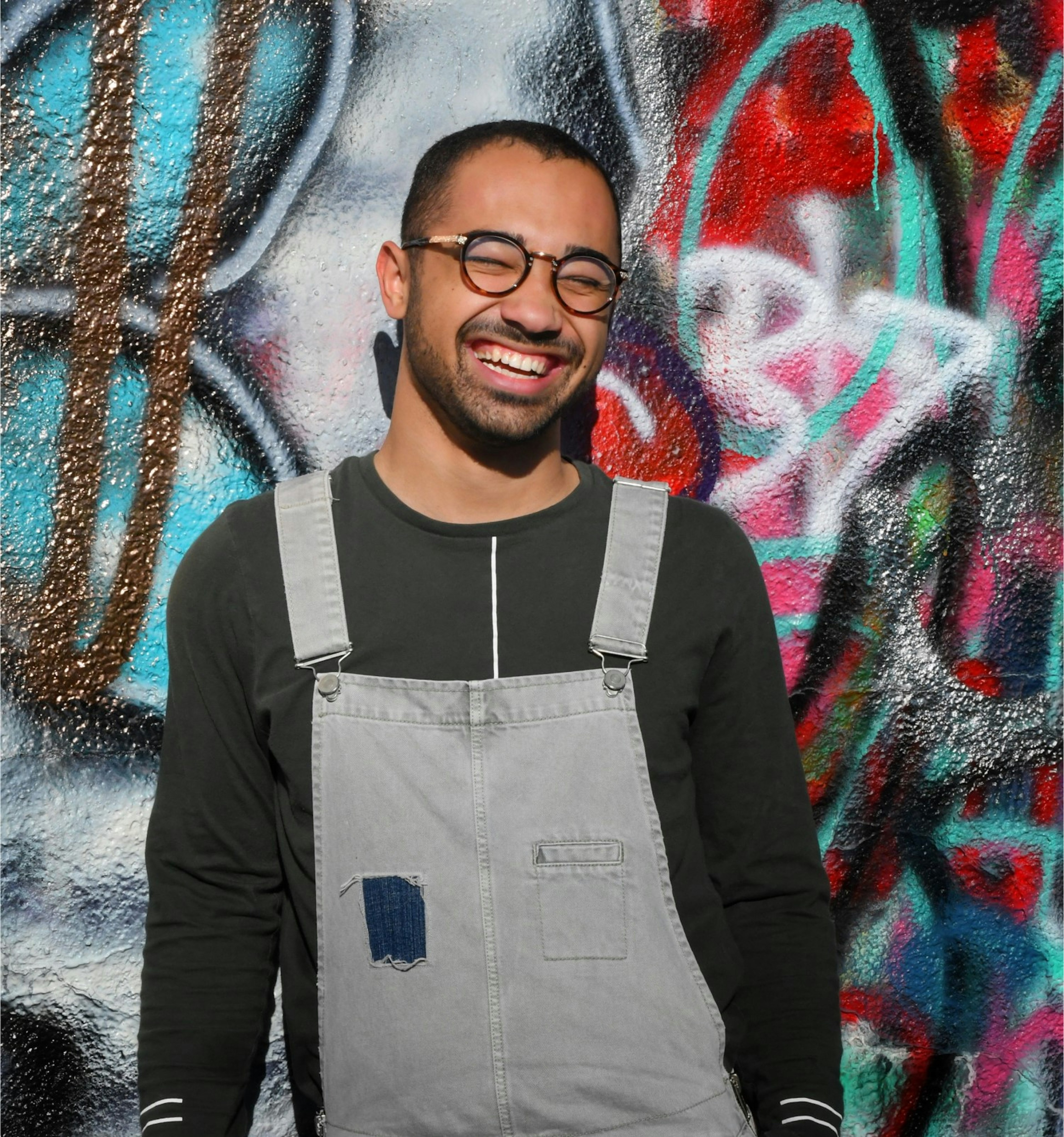 Happy man with overalls standing in front of a colorful wall.
